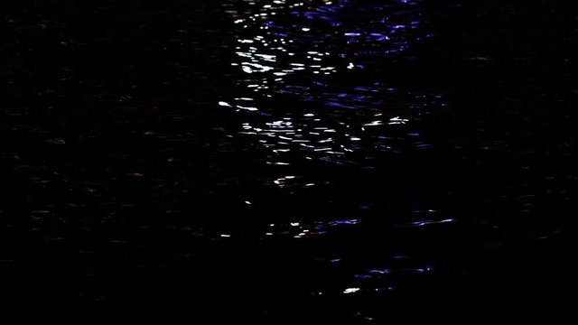 Dark sea water surface with colorful reflections of street seashore lightings at surface of black water. 4k video background.