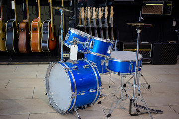 Fototapeta na wymiar Blue drums set in music instruments shop, small size. Guitars in the background