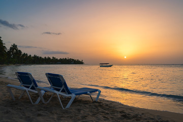 Two beach chairs and boat background on the tropical beach at sunset,Dominican republic,Bahia Principe beach.