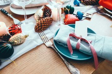 Fototapeta na wymiar Table served for Christmas dinner in living room. Close up view, table setting,plates, branch decoration, candles and gliterring toys on wooden table background. Winter decoration