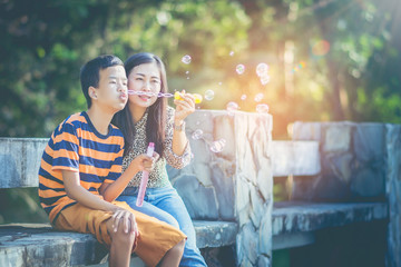 Beautiful Asian mother playing with her son is sick, autism. The boy are blowing bubbles with bubble fun with his mother's help and encouragement at all times. The atmosphere inside the park.