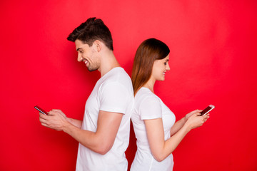 Photo of girlfriend boyfriend standing back to back chatting to each other browsing through telephone smiling toothily wearing white t-shirt isolated vivid color background
