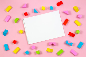 Colorful wooden building blocks and white blank open notebook on pink background. Top view