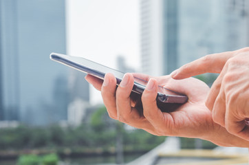 close up handsome man using hand typing smartphones and touch screen working search with app devices outdoor in city with sunrise and building background. 5G technology connecting the world.