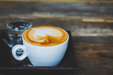 close up modern hot black coffee the cappuccino on wood background with coffee bubble foam pattern and texture in white cup looking and feel so delicious on glasses table in coffee shop.