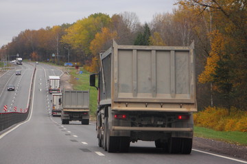 Gray dumper truck moving on asphalt road on autumn day, bulk cargo logistics