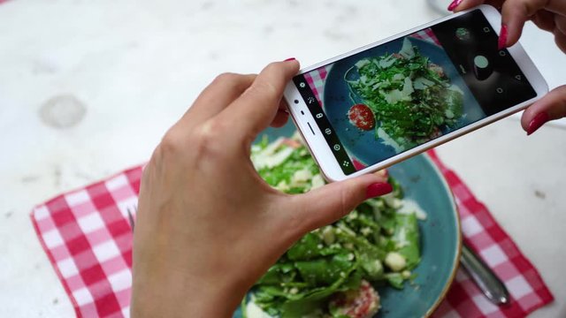 Closeup view of woman eating healthy vegetable salad in restaurant and making photos of it. Real time 4k video footage.