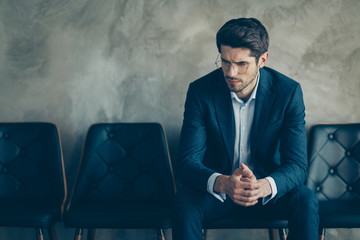 Portrait of sad guy feel nervous wait for meeting with new boss hr interview look pensive minded sit chair wear stylish blazer trousers isolated over grey color background