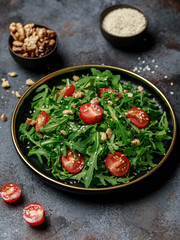 Healthy vegetable salad of fresh arugula, tomato and walnut on dark plate. Diet menu. Top view. Salad with arugula