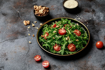Healthy vegetable salad of fresh arugula, tomato and walnut on dark plate. Diet menu. Top view. Salad with arugula