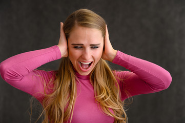 Close-up portrait of a pretty blonde girl with long curly hair standing in the studio on a gray background with emotions in different poses in a pink sweater. Beauty, Model, Cosmetics