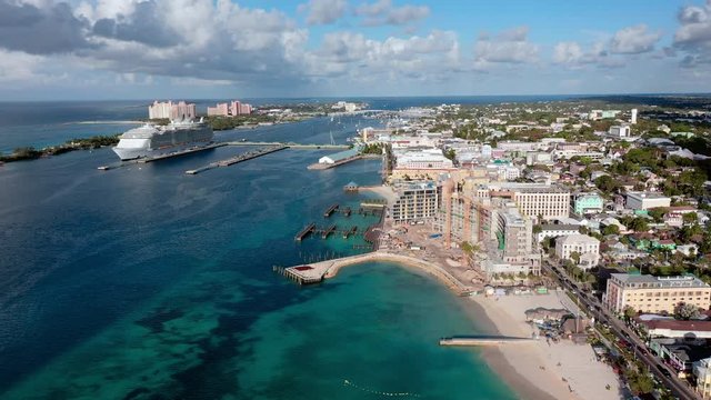 Aerial: Cityscape of Nassau, Beach, Hotels, and Huge Cruise Ship Docked Near Shore