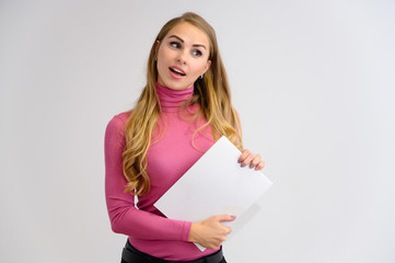 Naklejka premium Close-up portrait of a pretty blonde girl with long curly hair standing in the studio on a white background with emotions in different poses in a pink sweater with a folder in her hands.