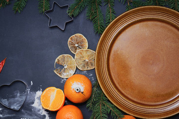 Spices flour orange pine tree branch and empty plate on a black board winter christmas background