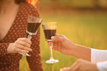 Happy young couple clinking wineglasses in park, closeup. Picnic season