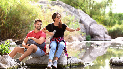 Young happy couple sitting on rock outdoors. Camping vacation