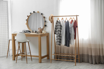 Hangers with stylish clothes on rack and dressing table in makeup room