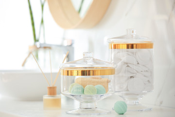 Fototapeta na wymiar Jars with cotton pads and bath bombs on white countertop in bathroom