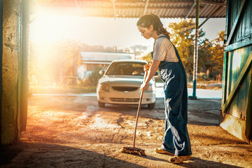 The concept of women's equality and feminism. A woman in a work uniform sweeps the working room with a broom. Setting sun