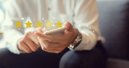 close up on businessman hand pressing on smartphone screen with gold five star rating feedback icon...