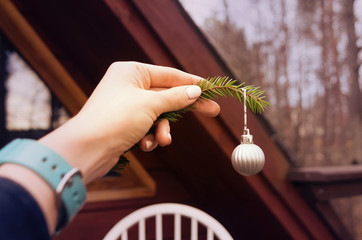 A female hand holding a fir tree branch with a silver bauble outdoors
