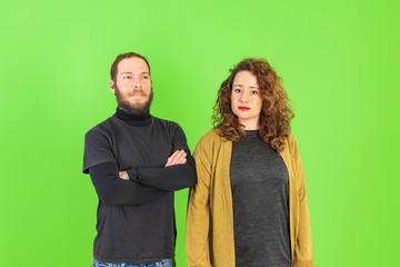 Beautiful young couple skeptic and nervous, disapproving expression on face with crossed arms over green background. Negative person.