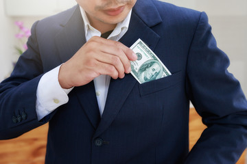 Close-up of young man in formalwear putting money in his pocket. Businessman pick up banknote from...