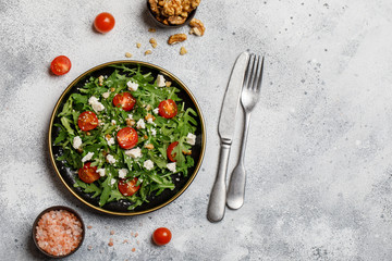 Healthy vegetable salad with fresh arugula, tomato, feta cheese and walnut on dark plate. Diet...