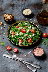 Healthy vegetable salad with fresh arugula, tomato, feta cheese and walnut on dark plate. Diet menu. Top view. Salad with arugula 