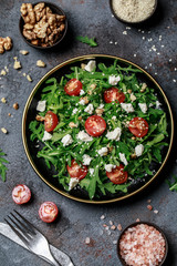 Healthy vegetable salad with fresh arugula, tomato, feta cheese and walnut on dark plate. Diet menu. Top view. Salad with arugula 