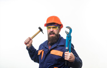 Bearded man with repair tools in hand. Repair service. Worker in helmet with pipe wrench. Bearded man in construction helmet. Uniform. Mechanic. Plumbing and renovation. Hammer hammering. Pipe wrench.