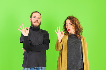 Young beautiful couple over green isolated background doing ok gesture with hand.