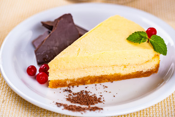 Cheesecake decorated with chocolate pieces, cranberry and mint leaves on white plate