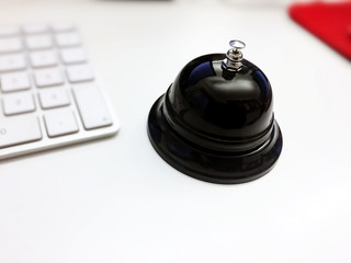 black bell of a hotel reception near a white computer keyboard