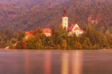 Picturesque morning view of Bled Lake and Pilgrimage Church of the Assumption of Maria on small island against autumn forest. Famous touristic place and romantic travel destination in Slovenia