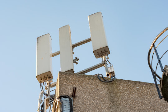 Isolated image of 4G and wireless communications mast seen atop a private office roof. Detail of the cables can be seen, and part of a stairwell on the left.
