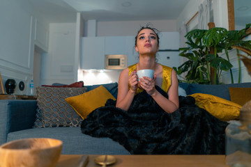 Young attractive anxious woman watching TV series and drinking hot tea. Concept of cold autumn or winter time spending.