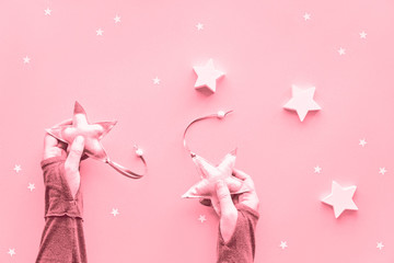 Creative pink monochrome Christmas flat lay on paper background. Hands holding soft textile stars, flat lay with large and small paper stars.