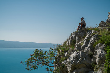 Bearded man is sitting on a rock above the sea and looking deep