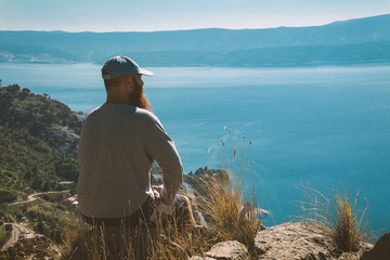 Hiking man is sitting on a cliffs edge and looking to the other sea side