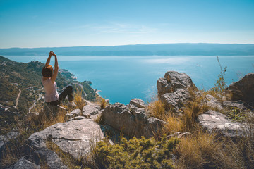 Young woman is resting on a stone at the top of rock above the Adriatic sea