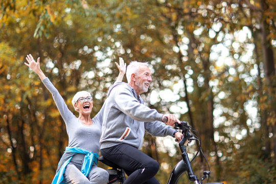 Senor copule in the park, he drive bicycle and she is sitting back and smile