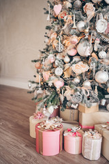 Beautiful Christmas gift boxes on floor near fir tree in room. Decorated Christmas tree in soft pink colors with snow covered branches. New Year presents