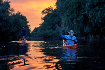 Two men paddling on SUP (stand up paddle board, paddleboard) and kayak in Danube river against the...