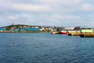 Fototapeta na wymiar Looking in toward the town of Port-aux-Basque, Newfoundland Labrador, from the harbour. Commercial buildings on the waterfront, boats on the dock, houses on the hill.