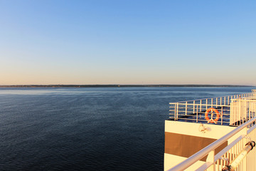 Top deck of a ship at sea, early morning. Morning sun, ocean in the background, land just visible on the horizon.