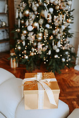 Golden present box against the background of a Christmas decorated tree in warm golden hues. New Year and Christmas concept. Festive postcard