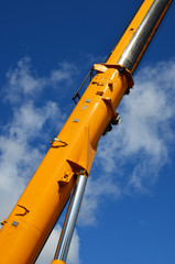 Vertical photo of yellow lifting crane arm against the blue sky on sunny day