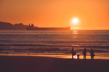 Obraz premium A family facing the sea on a sunset with the sun hiding behind the side of a boat