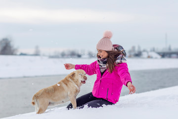 Young woman playing with her labrador ritriever in the snow on winter day